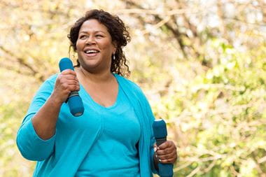 A curvy woman of color exercising outside with hand weights