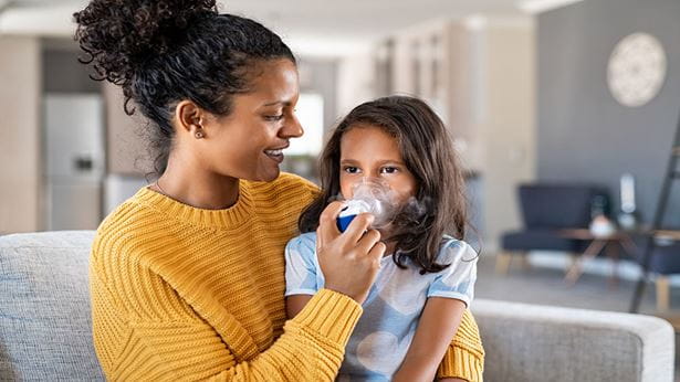 image of a mother helping her daughter use her asthma inhaler