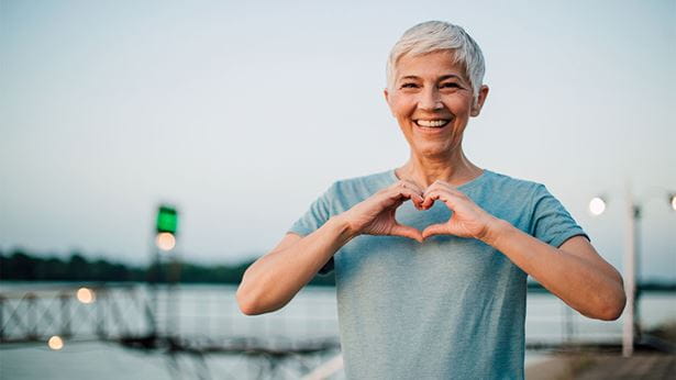 Women with white hair and blue t-shirt holding her hands in the shape of a heart