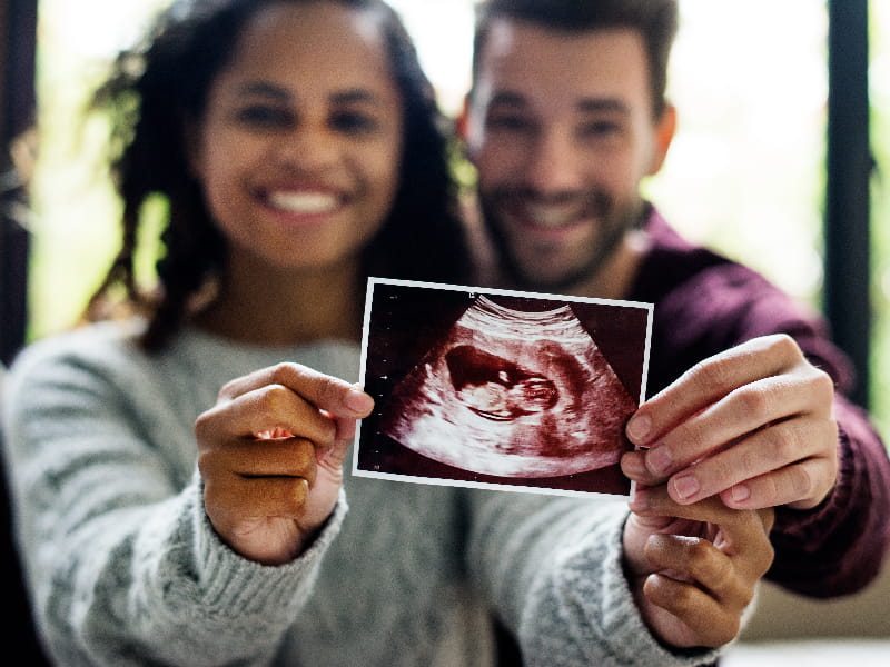 a couple holding an ultrasound image showing a baby fetus