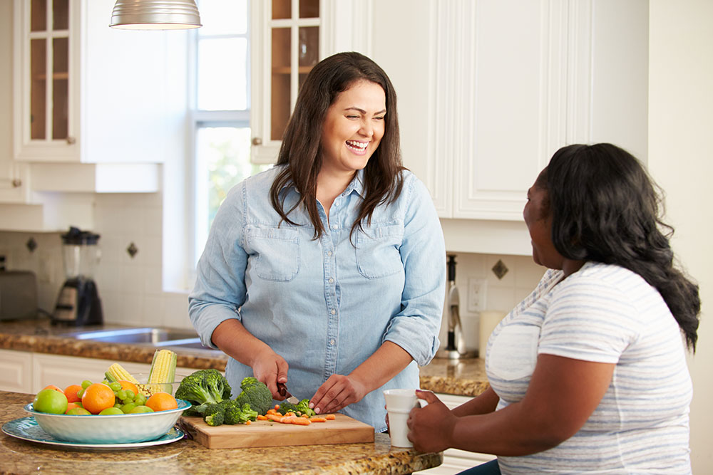 Two curvy women making a healthy dinner of vegetables and chatting